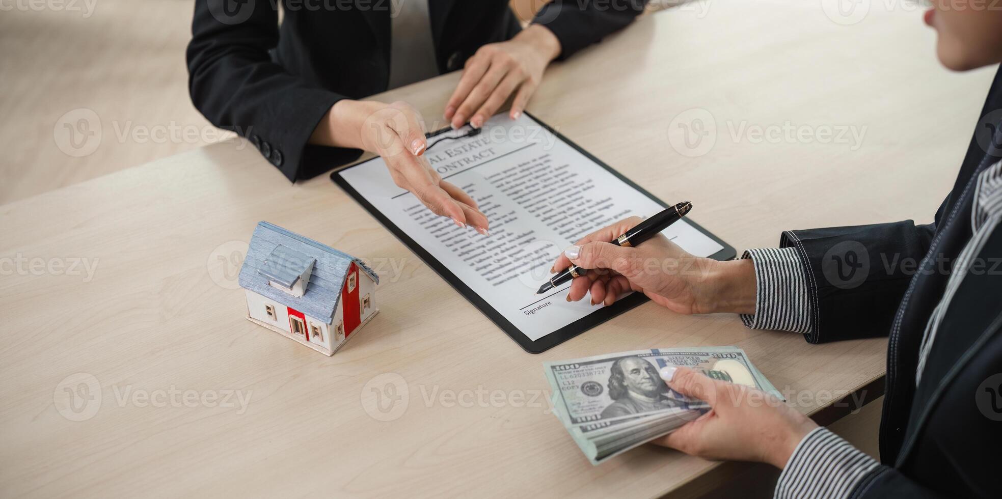 Real Estate Agents Discussing Home Buying and Selling Contracts with Money and Model House on Desk photo