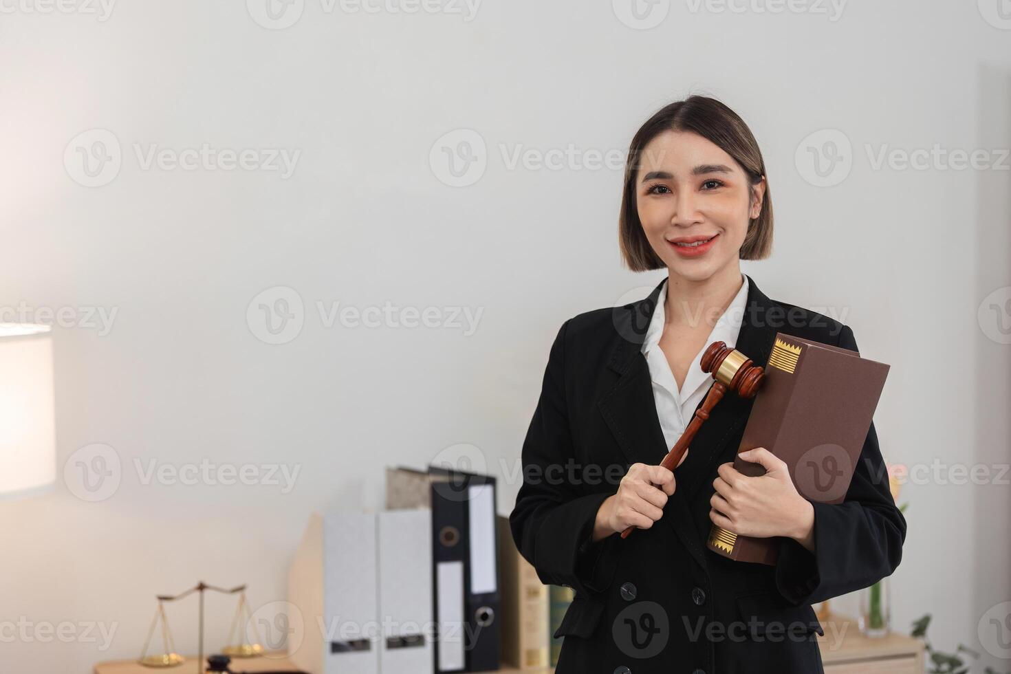 Confident Young Lawyer Holding Gavel and Legal Book in Modern Office Setting, Ready to Tackle Legal Challenges photo