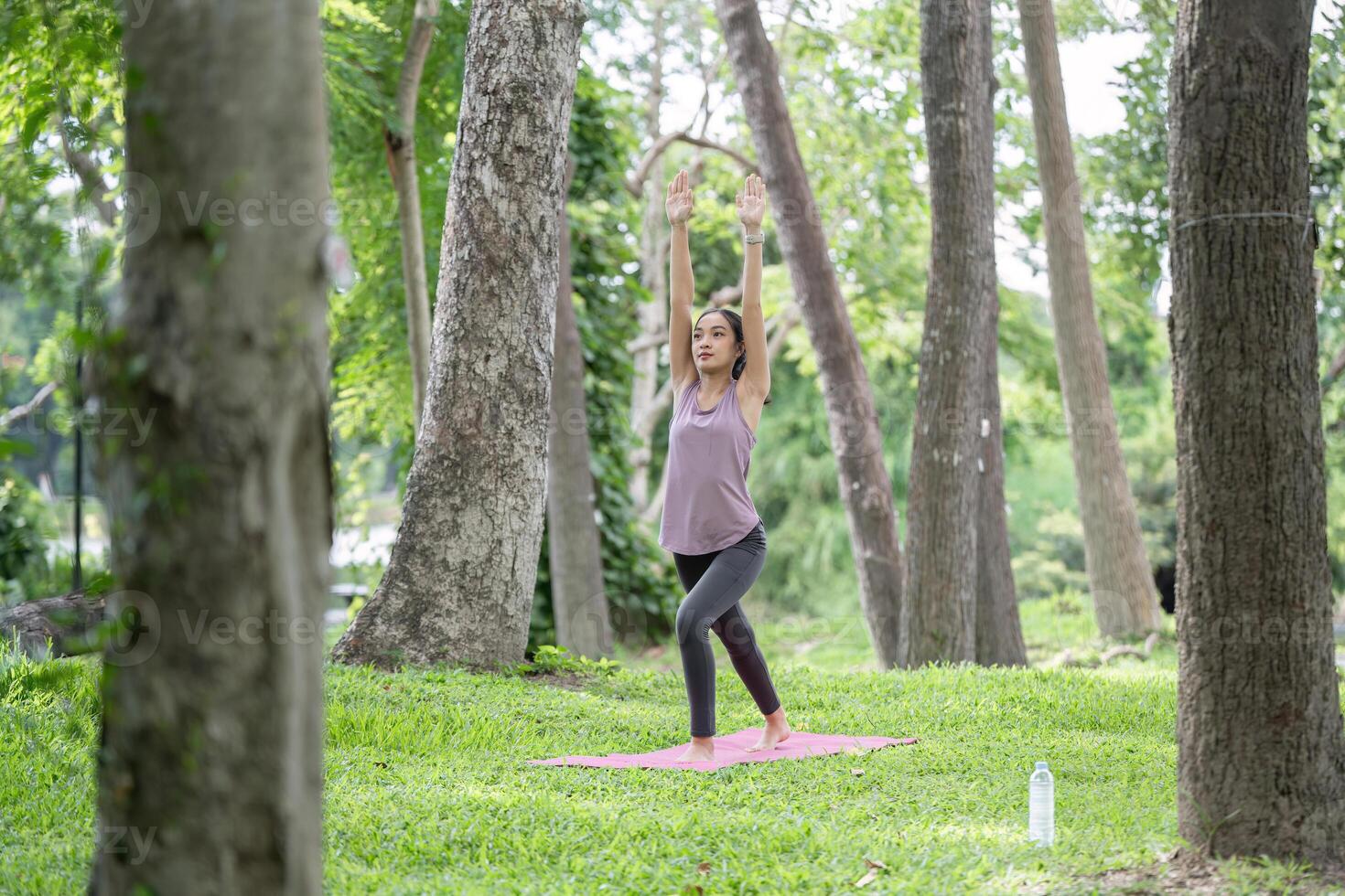 Young Healthy Woman Practicing Yoga Outdoors in a Lush Green Park Surrounded by Trees and Nature photo