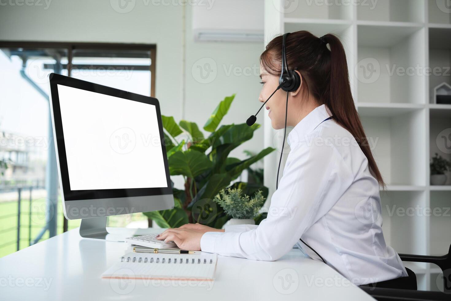 Young call center woman engaging with online customer in modern office Provide customer support via a computer with a white screen photo