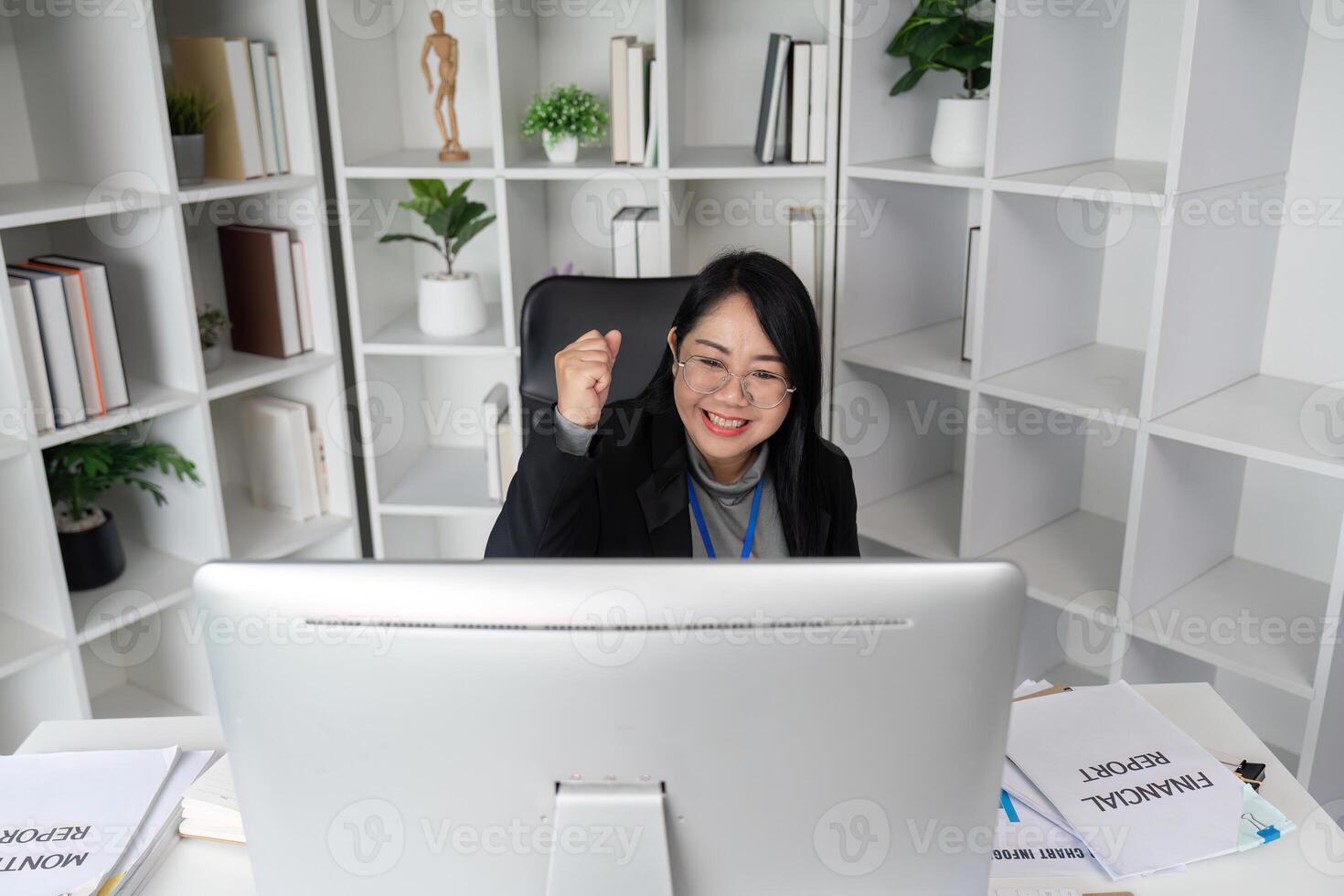 Successful Businesswoman Working on Computer in Modern Office with Bookshelves and Plants, Celebrating Achievement photo