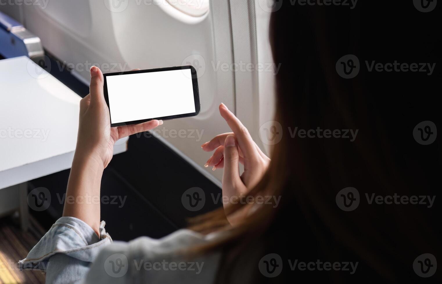 Young Businesswoman Using Smartphone While Traveling by Plane for Work, Focused on Blank Screen, Modern Technology in Business Travel photo