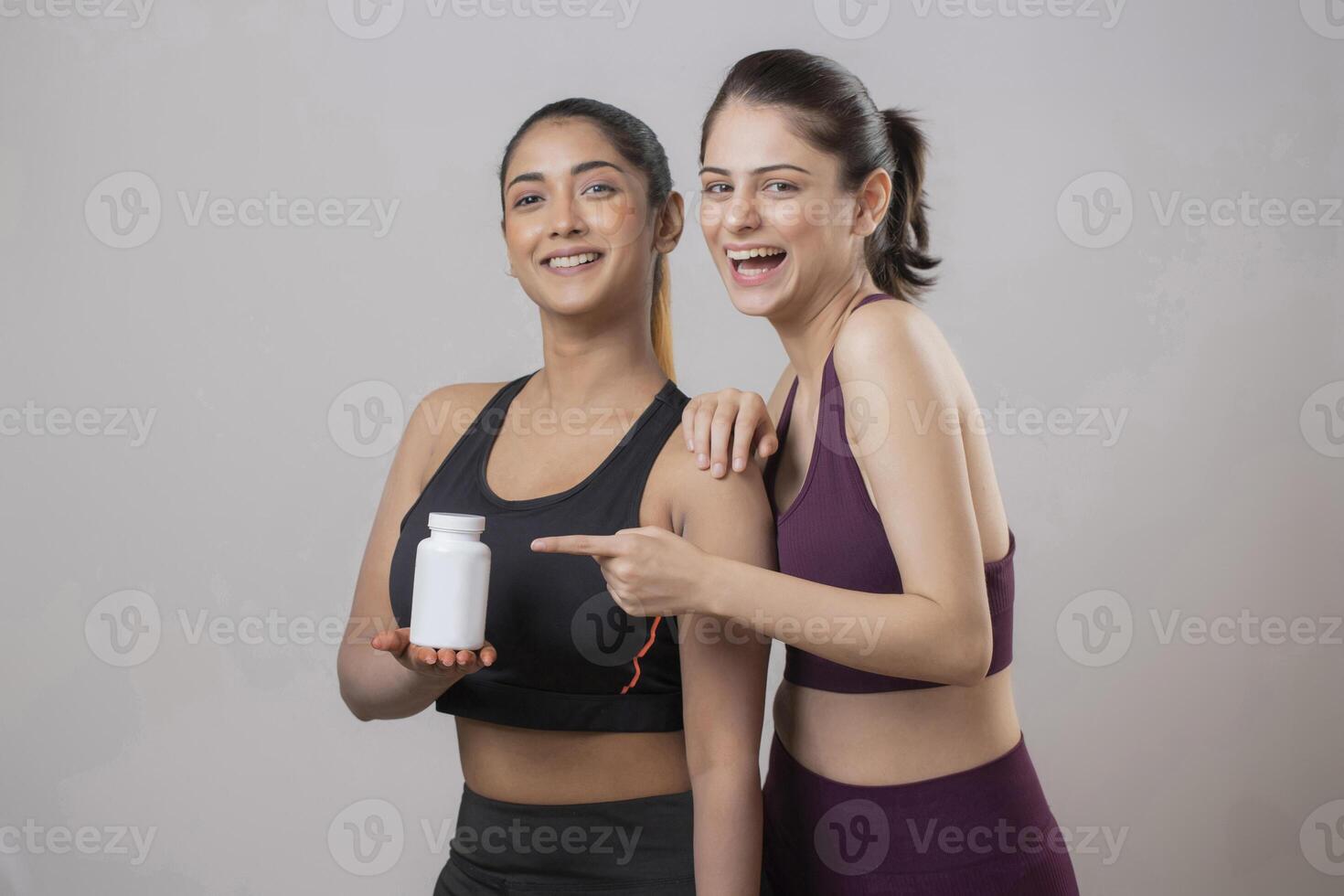 Two Female Models Are Standing With One Holding Pill Bottle While Another Points Her Finger At The Bottle photo