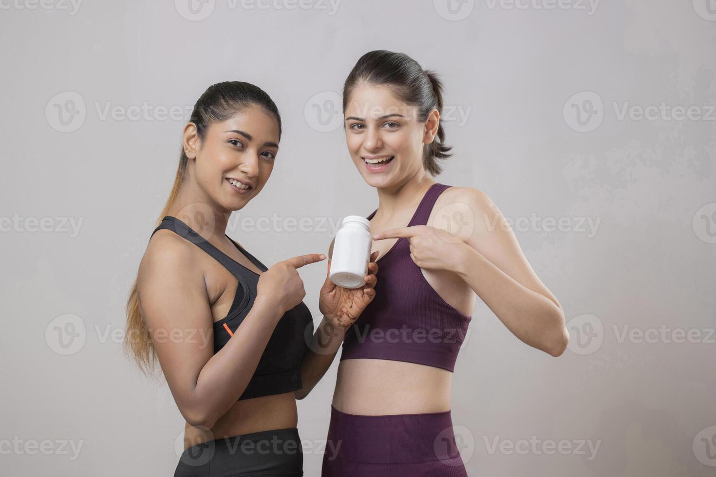 Two Cute Females Are Pointing Their Fingers At A Tablet Bottle While Looking At The Front Camera photo