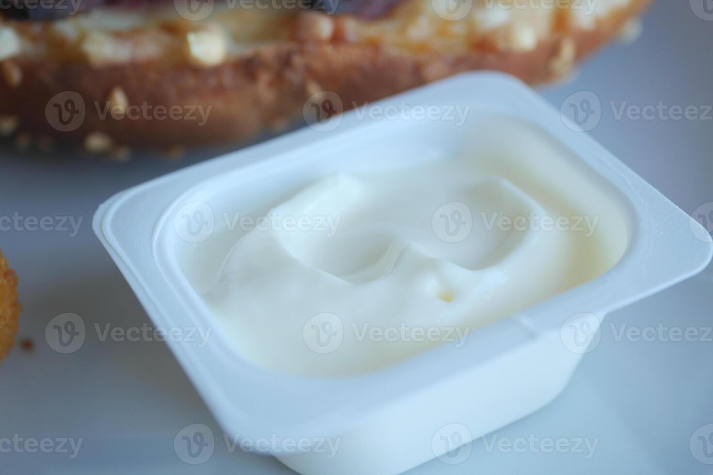 A Creamy White Sauce in a Plastic Container is Positioned Next to Delicious Food Items photo