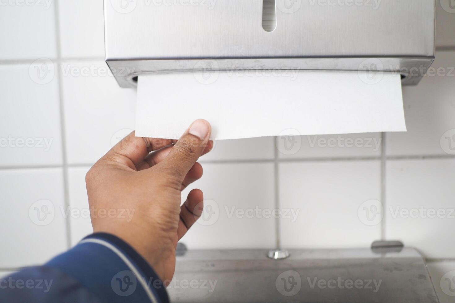 Hand Using Paper Towel Dispenser in a Hygienic Public Restroom with Clean White Tiles photo