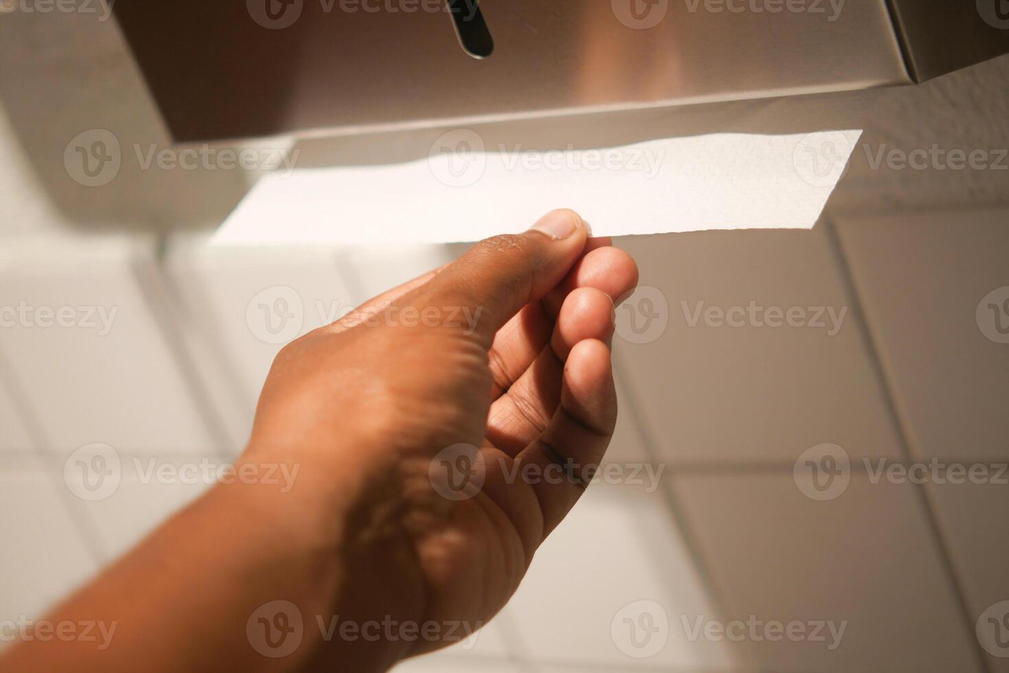 Hand Using Paper Towel Dispenser in a Hygienic Public Restroom with Clean White Tiles photo
