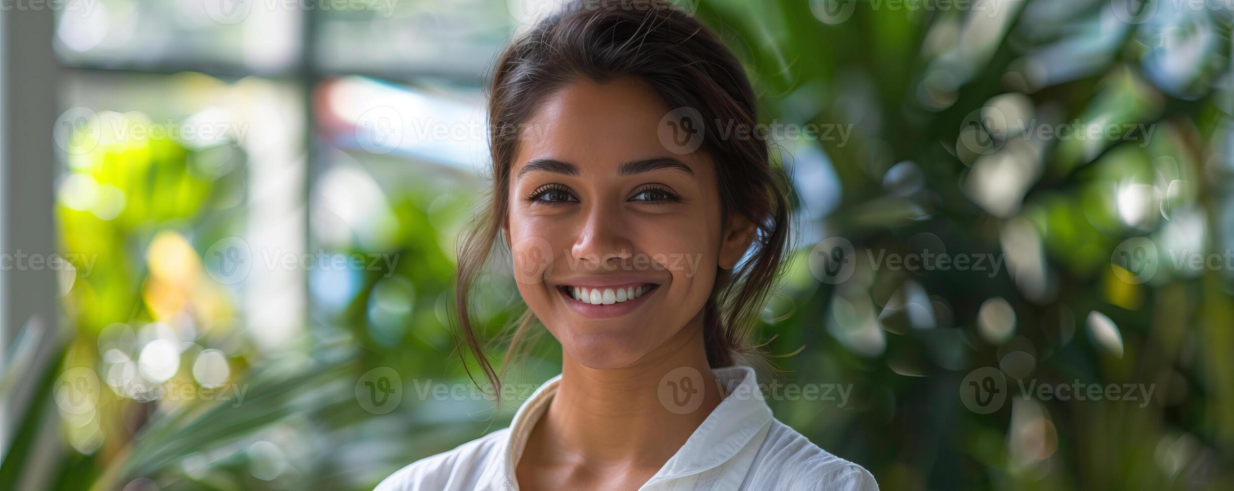 Happy young woman smiling in front of a blurred background of foliage photo
