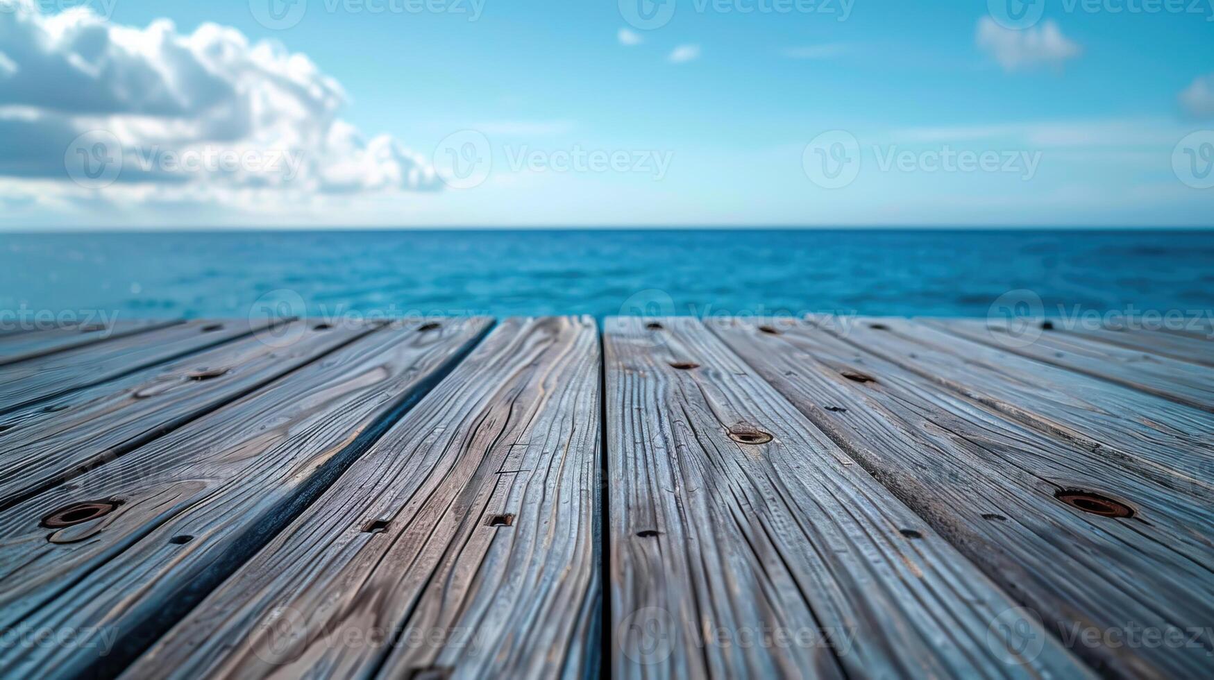 A wooden dock extending out into a calm blue ocean with white clouds overhead. photo