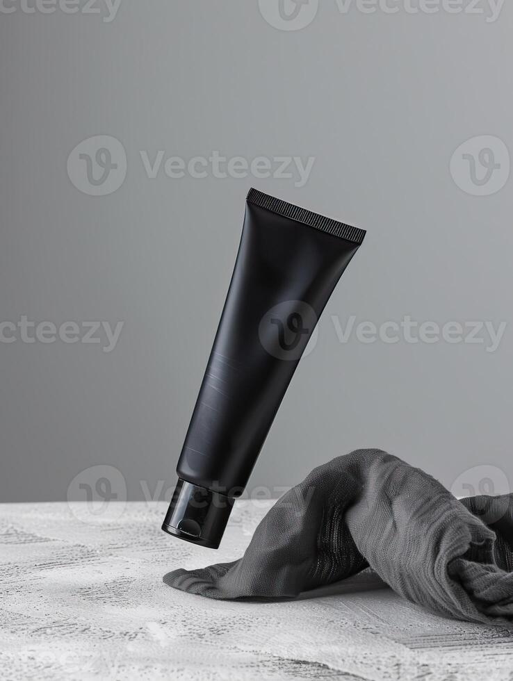 A black tube of face cream is suspended in mid-air above a gray cloth. photo