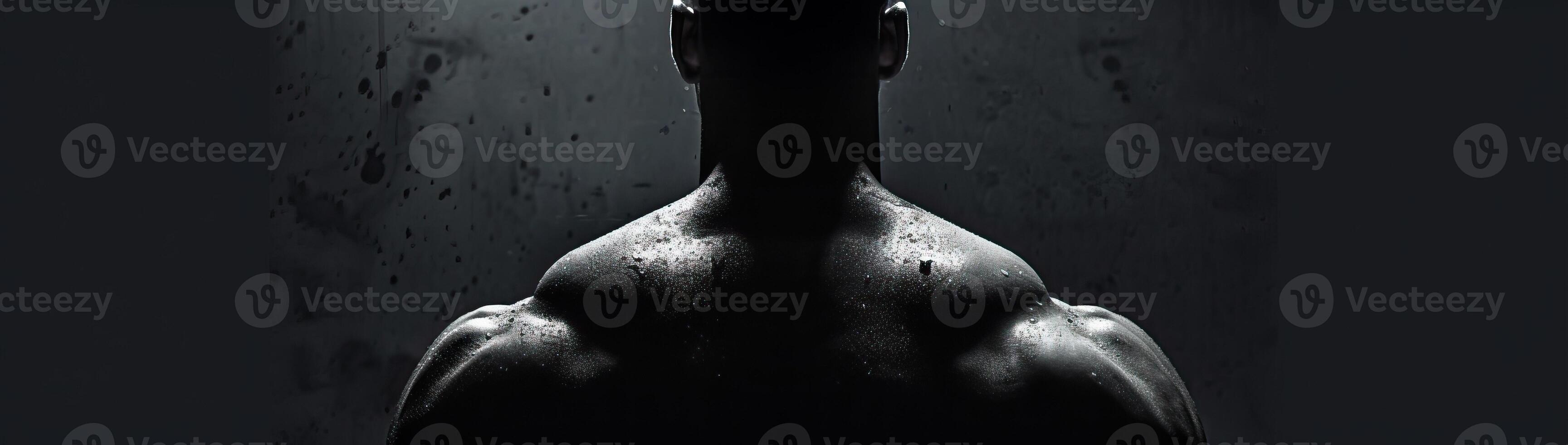 A powerful silhouette of a muscular man showcasing back muscles in low light, emphasizing strength and fitness in a dramatic and dark setting. photo