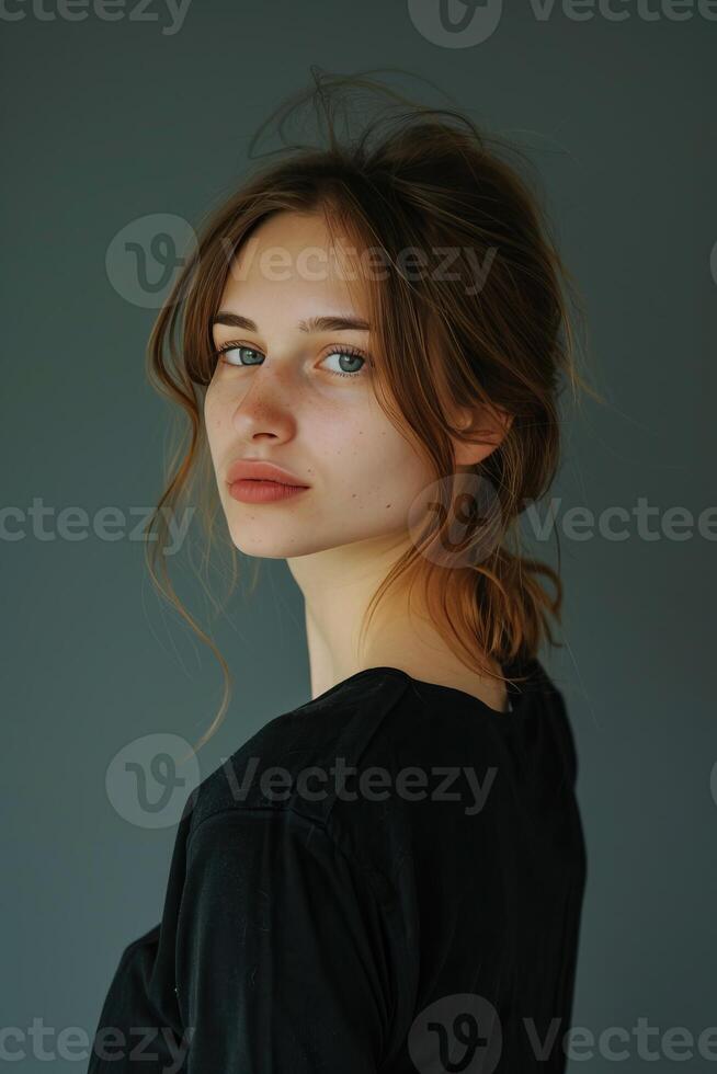A beautiful young woman with long brown hair and green eyes is looking over her shoulder at the camera. She is wearing a black t-shirt and has a soft smile on her face. photo
