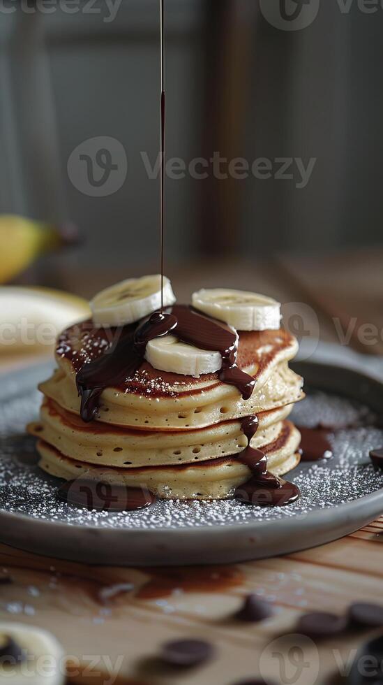 A decadent stack of pancakes topped with sliced bananas and drizzled in chocolate syrup. photo