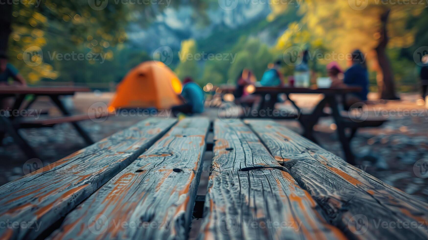 Blurred background of people camping in the forest with wooden picnic tables and a tent, capturing the essence of an outdoor adventure. photo
