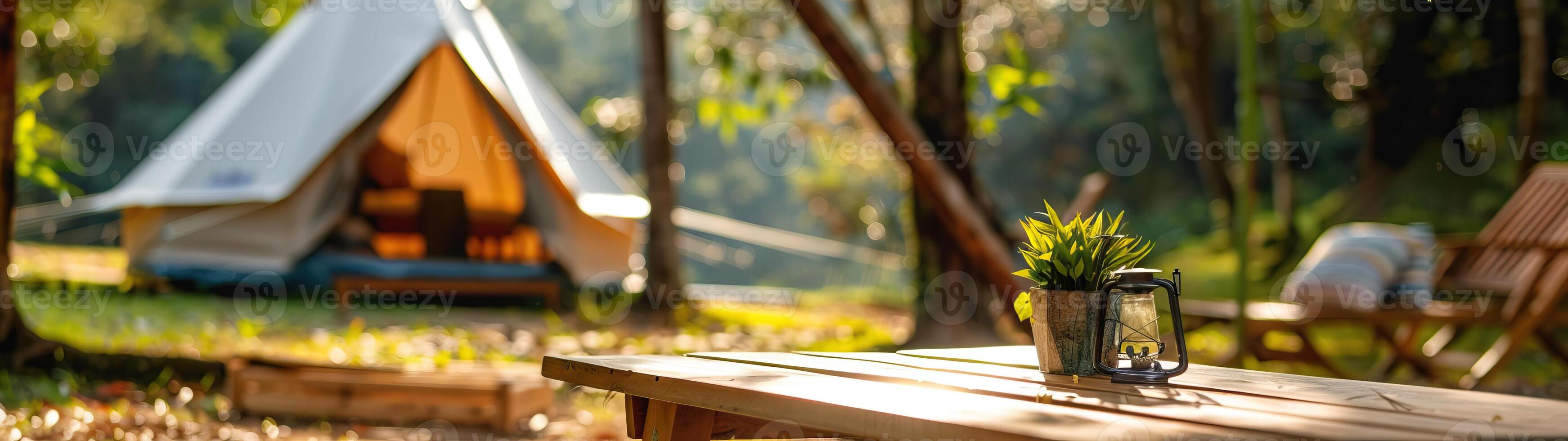 A serene outdoor camping site featuring a tent, a wooden table with a plant, and natural surroundings bathed in warm sunlight. photo