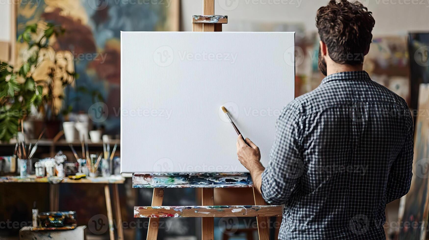 Creative artist standing in front of a new white canvas on an easel, brush in hand, ready to start painting, modern art studio, focused and inspired photo