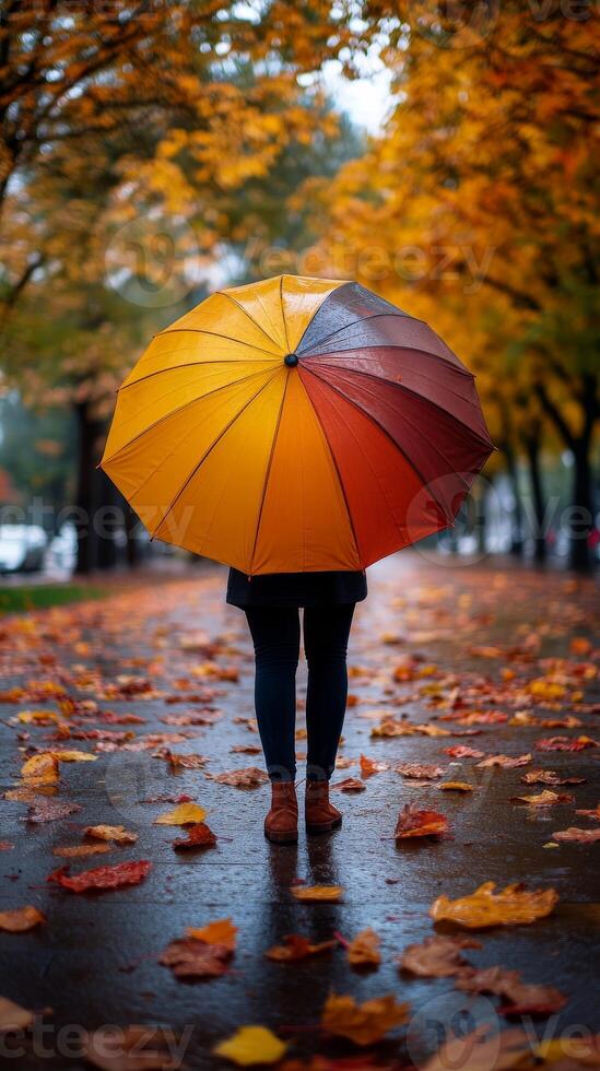 Top view of person under bright umbrella, with autumn fallen leaves on the sidewalk. Vertical banner photo