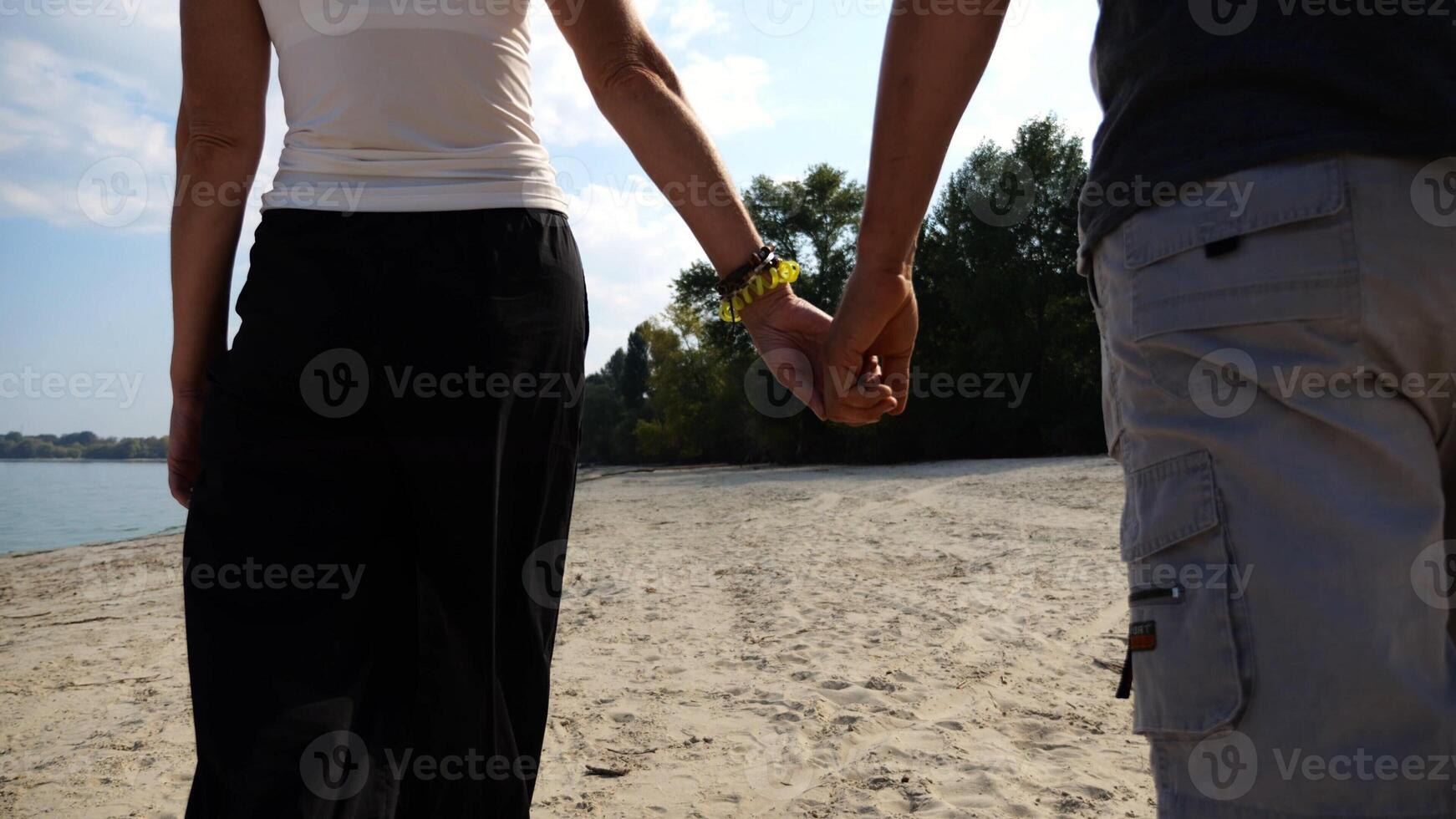 Couple holding hands of each other and walking at coast. Happy pair going along seashore at sunny day. Lovers spending time together at resort. Concept of vacation or holiday. Slow mo photo