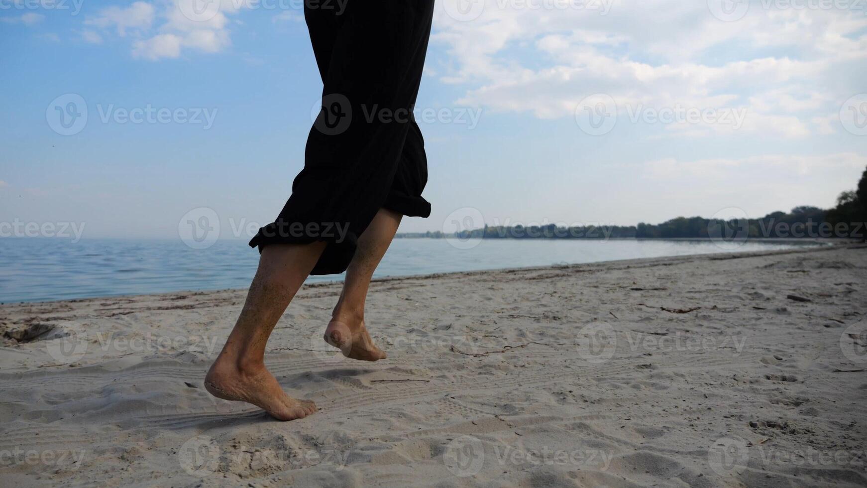 Bare feet of adult woman jogging on sand at the beach with seascape at background. Female legs running along sea shore. Happy lady spending time near ocean coast. Concept of summer vacation photo