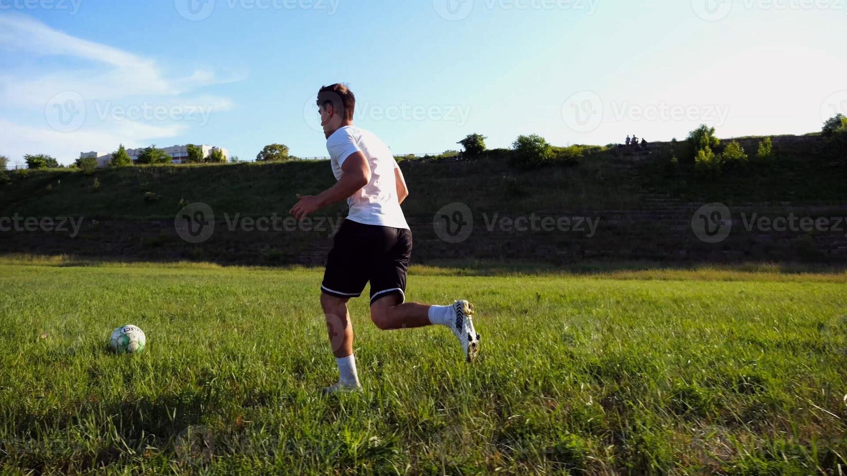 Professional footballer in uniform shows tricks with ball while running at green field. Sportsman kicks ball during jogging at meadow on sunny day. Young man training at stadium. Freestyle football photo