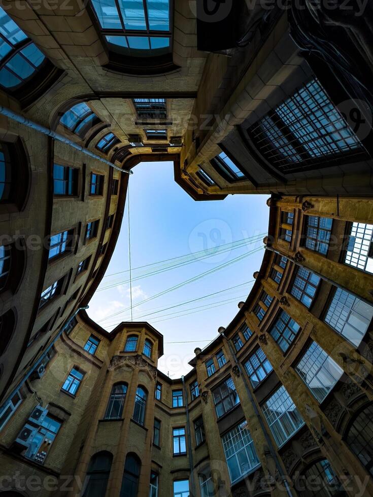 A dramatic upward view of a historic courtyard with curved architecture, emphasizing the symmetry and intricate details of the building against a clear blue sky. The image captures the unique photo