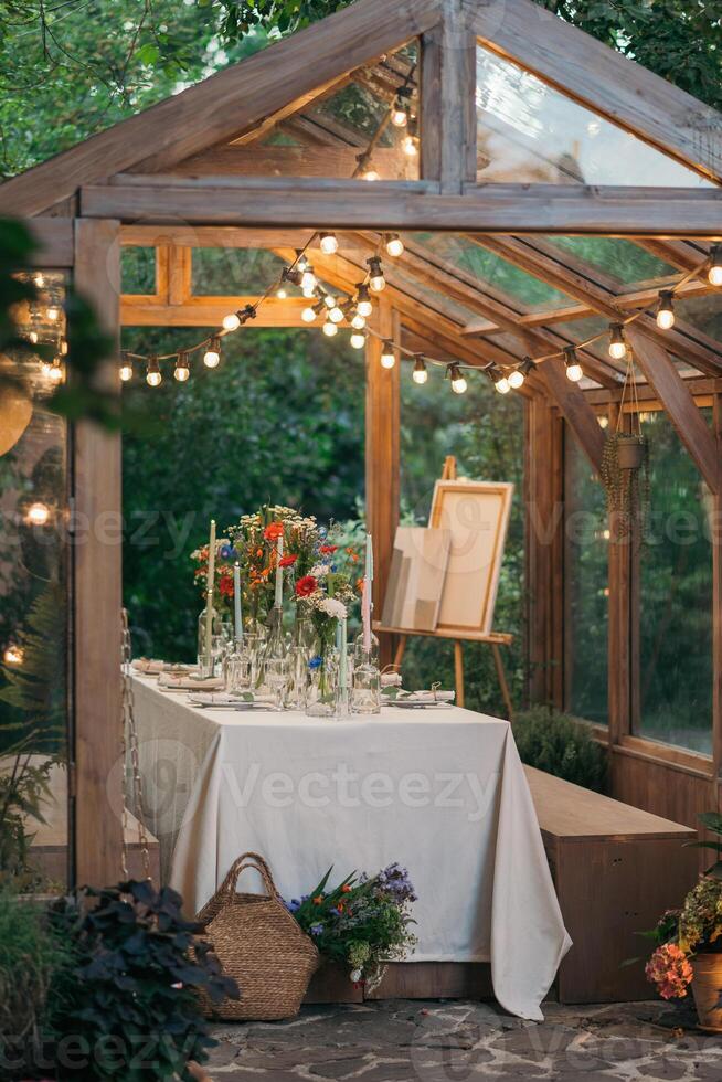 decorated greenhouse in trendy wedding setting with dinner table, candles and candle lights. photo