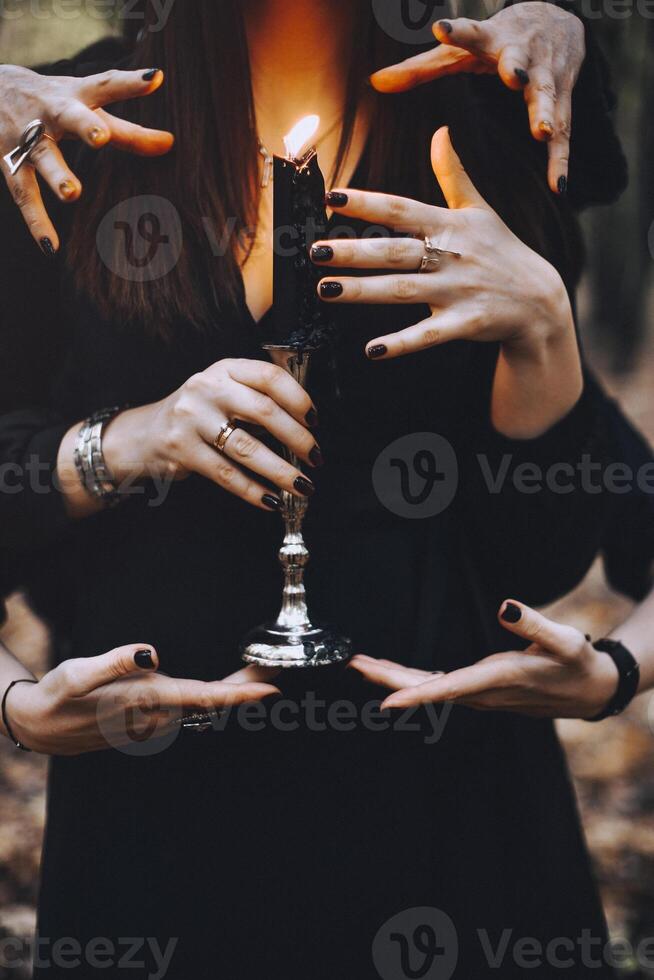 Witch with burning candle being touched by many hands during magic ritual in dark autumn forest photo