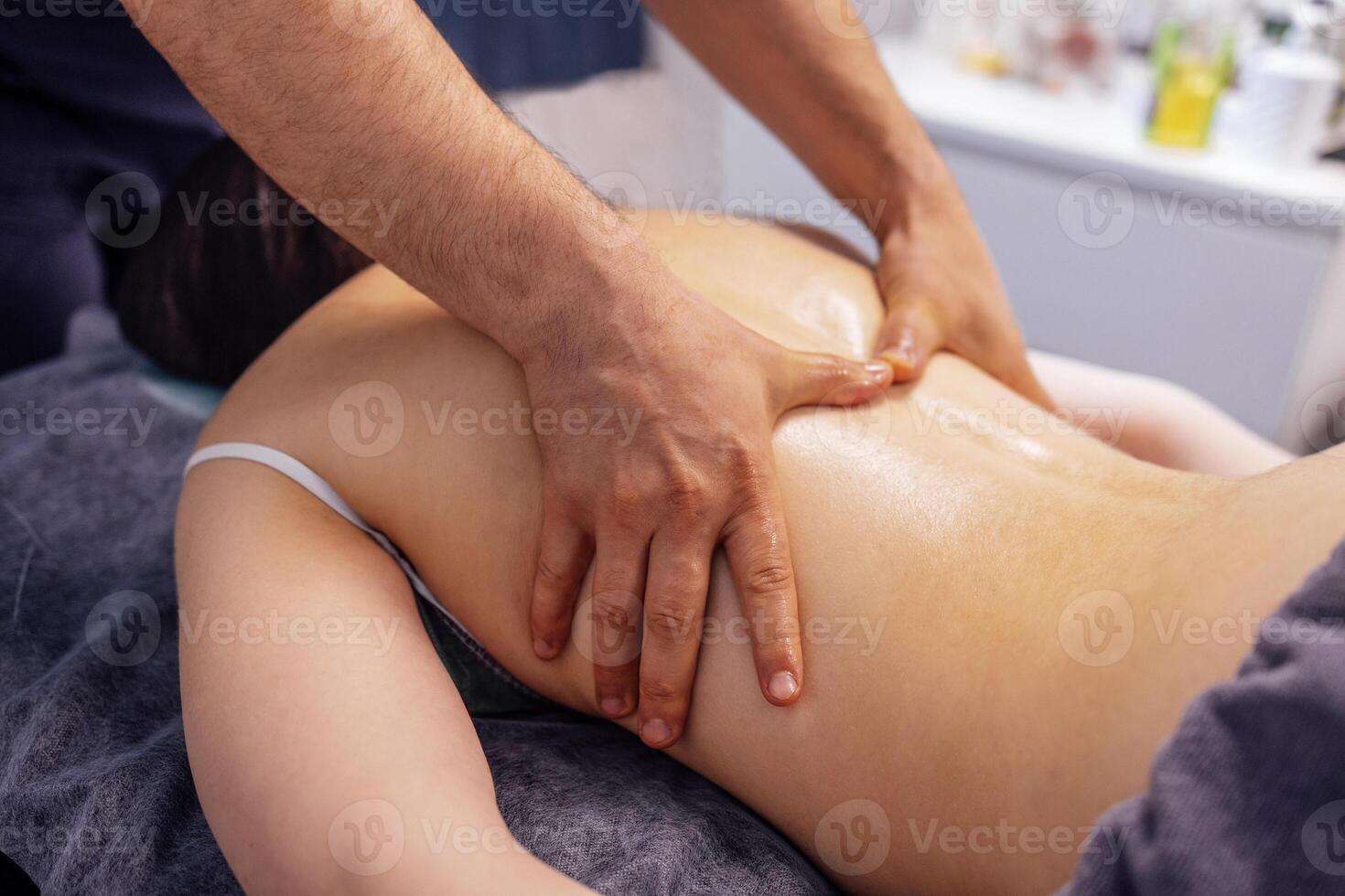 Young caucasian woman getting back massage in spa salon. The strong hands of the masseur touch the female client back. photo
