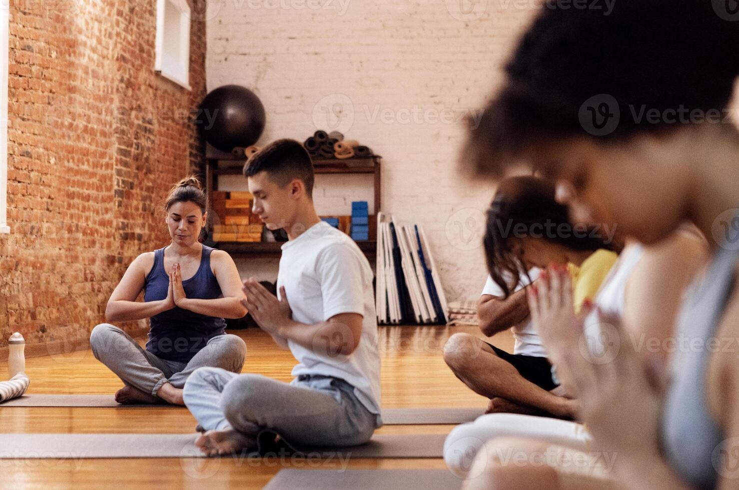 A group of multiethnic athletes sit on mats and meditate. The end of fitness classes and relaxed people in sports clothes in the lotus position in the gym. photo
