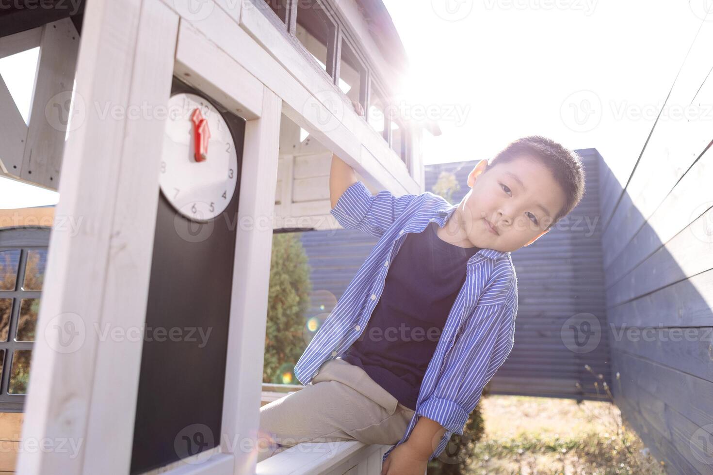 An Asian little boy looks out from a children wooden house. A Korean child is playing in the backyard. photo