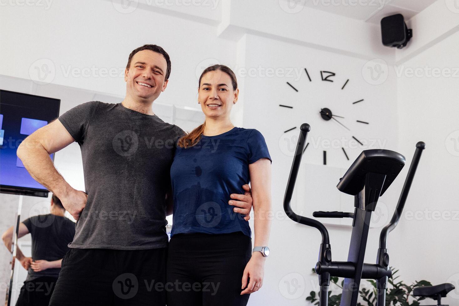 Happy young couple posing in wet shirts after ems workout. Man and woman are smiling and hugging in the gym or fitness club. photo