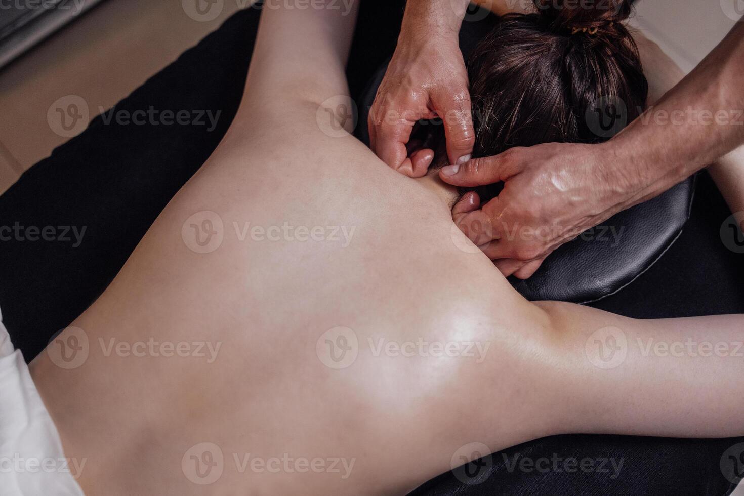 Happy young caucasian girl getting back massage in spa salon. Neat hands of male masseuse photo