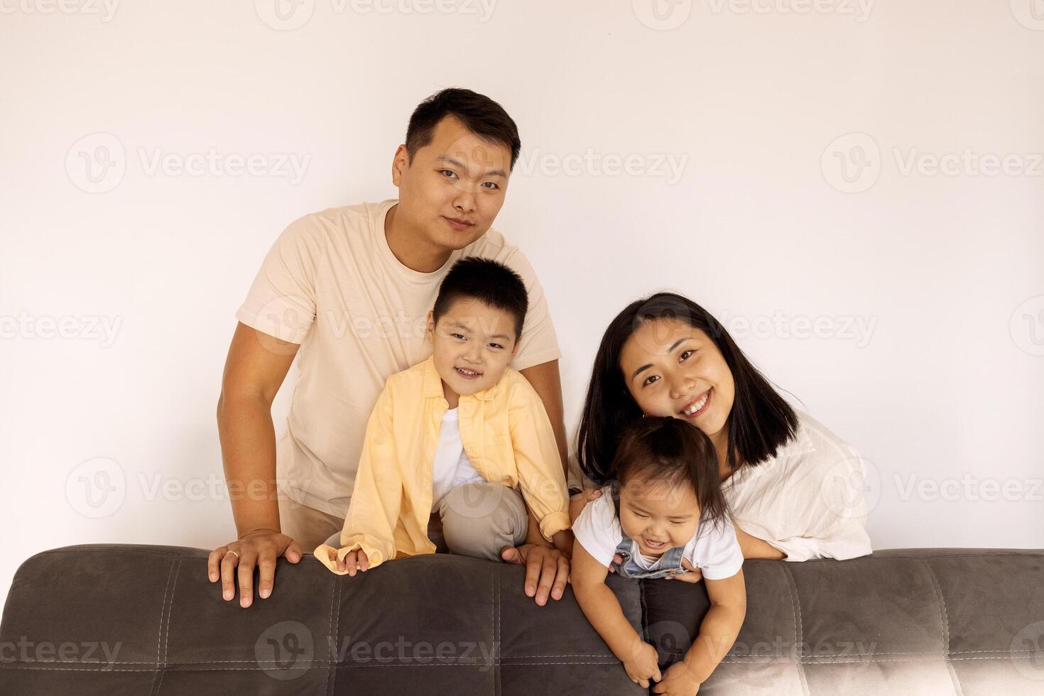 Happy Asian family at home. A Korean couple and their cute little kids on the sofa in the living room. photo