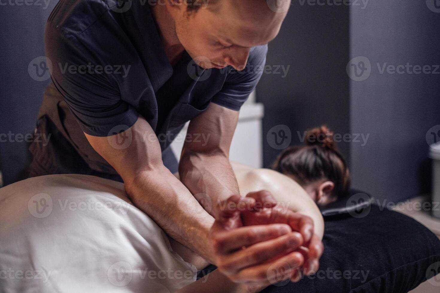 Happy young caucasian girl getting back massage in spa salon. Neat hands of male masseuse photo
