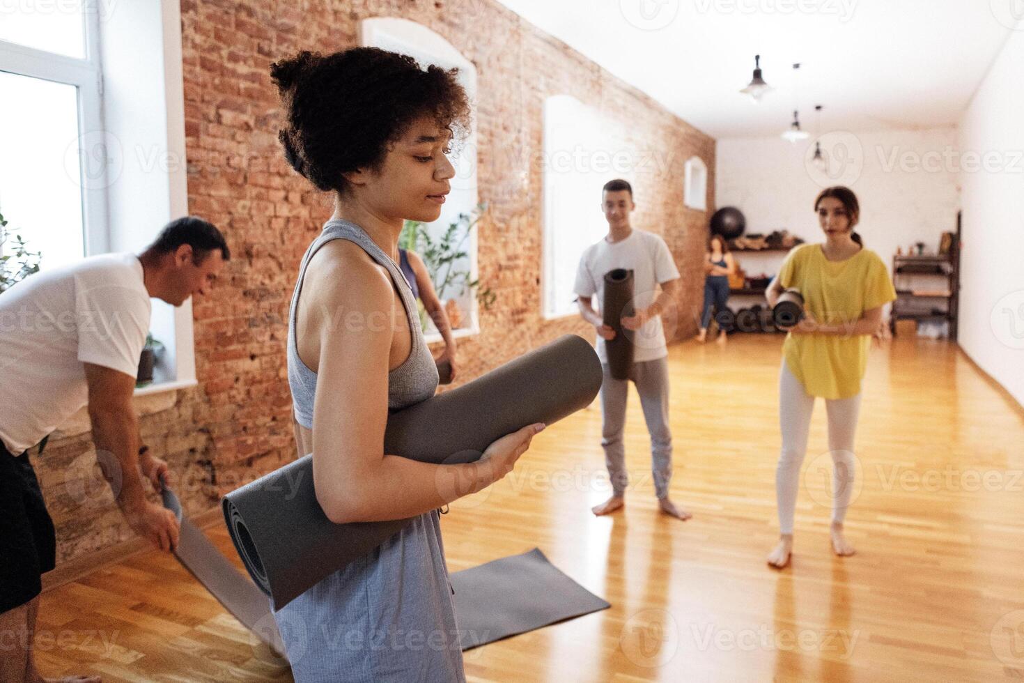 A group of multiethnic athletes roll up mats after yoga classes. The end of fitness classes and relaxed people in sports clothes in the gym. photo