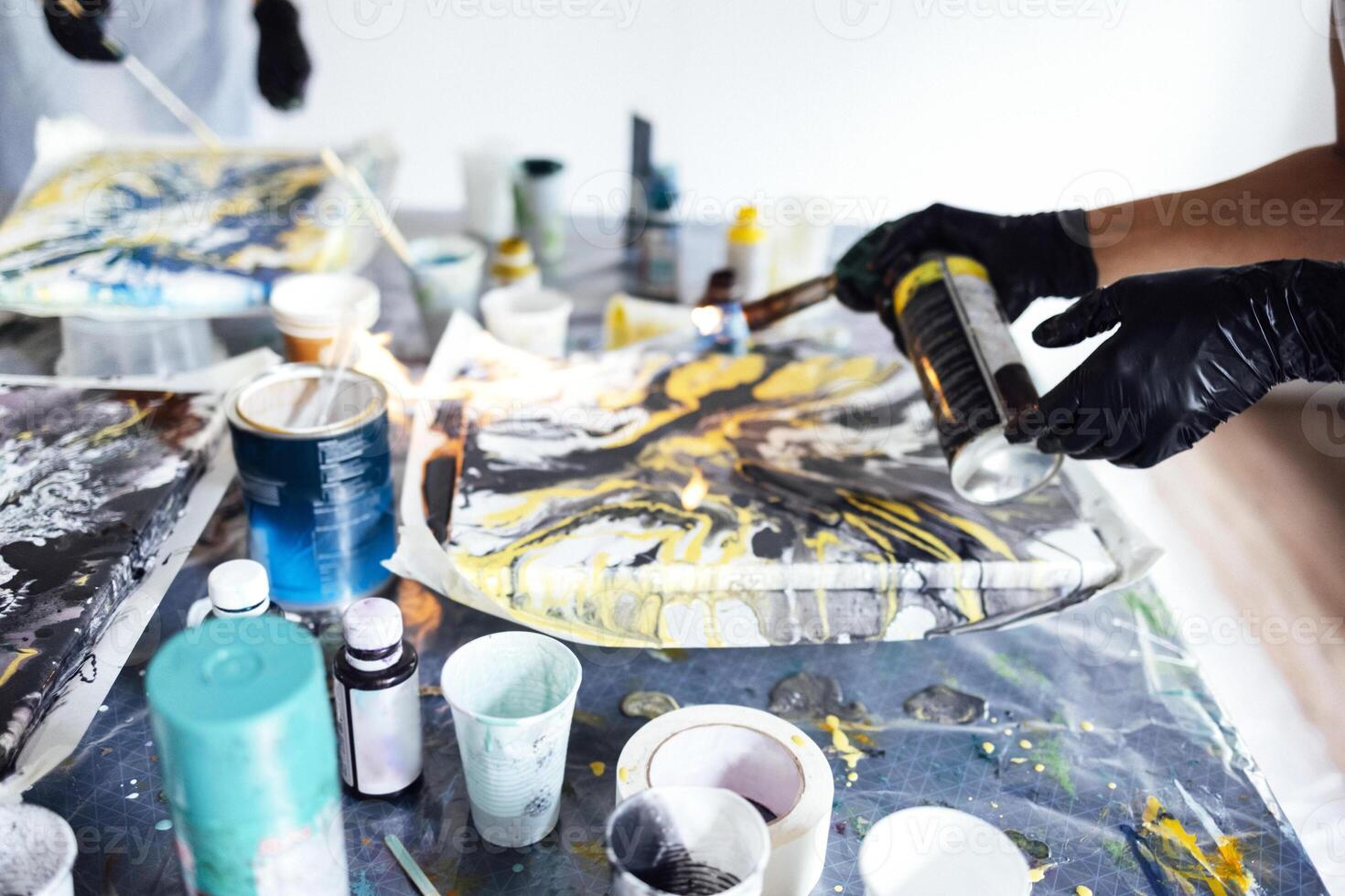 A woman uses a gas burner to draw in Fluid Art. Process of creating a painting with liquid acrylic paints. photo