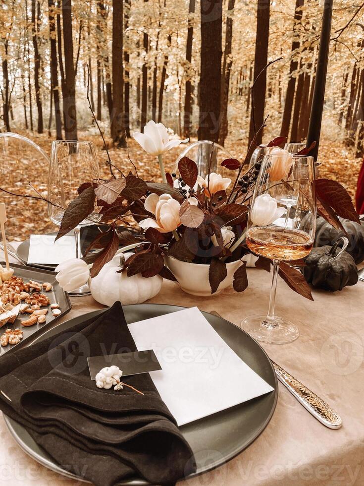 Table serving outdoors in the autumn forest. Black plate and napkin, card, fork, glass of champagne. Nuts and cheese on a plate for snacks. photo