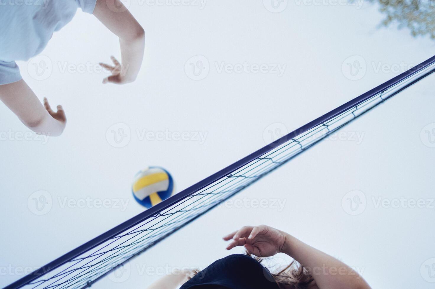 Volleyball game in summertime. Extreme bottom view of the net, multi colored ball and two players. photo
