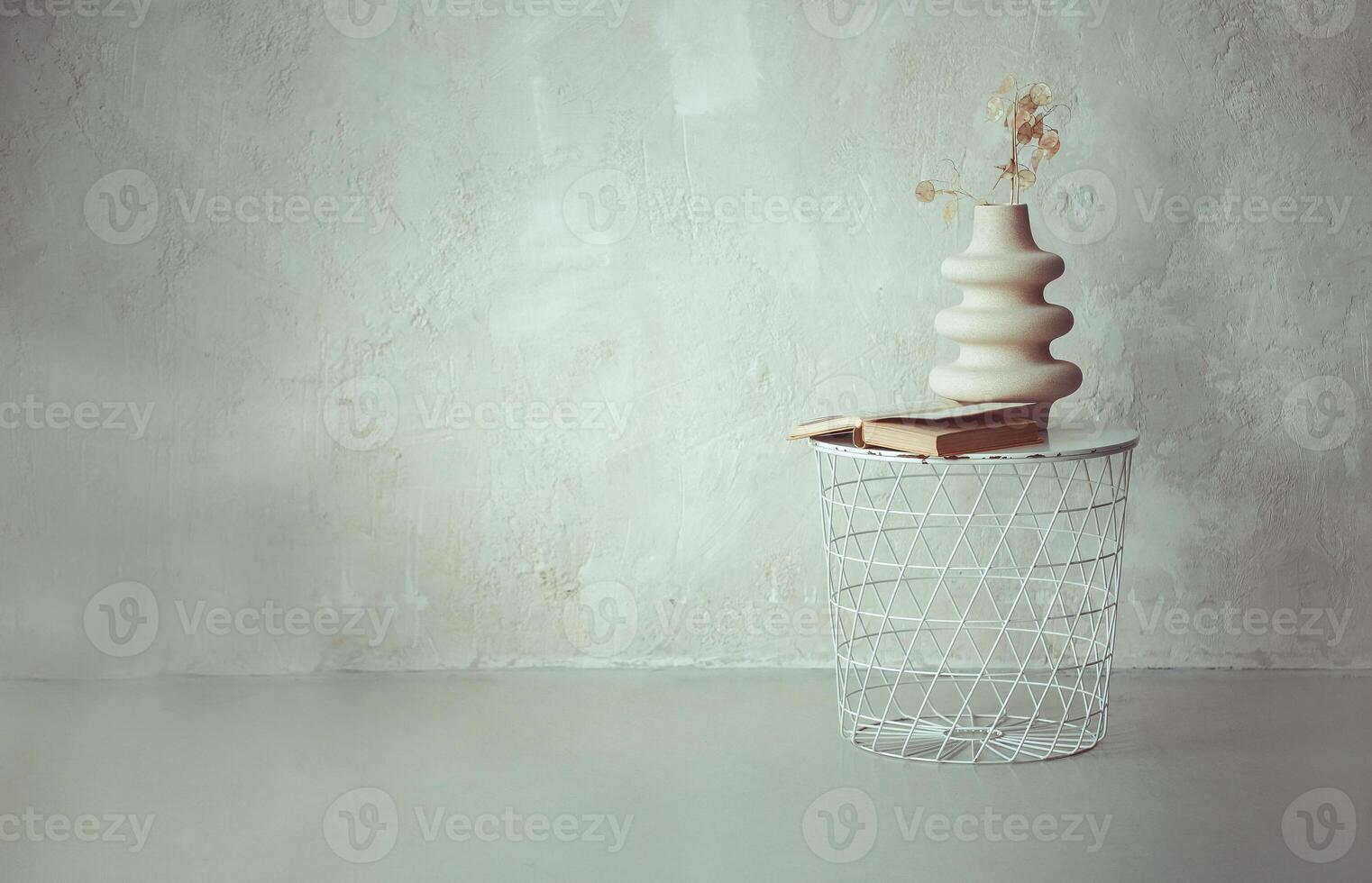 Book and dried twig in ceramic vase on white metal round bedside table against beige concrete wall photo