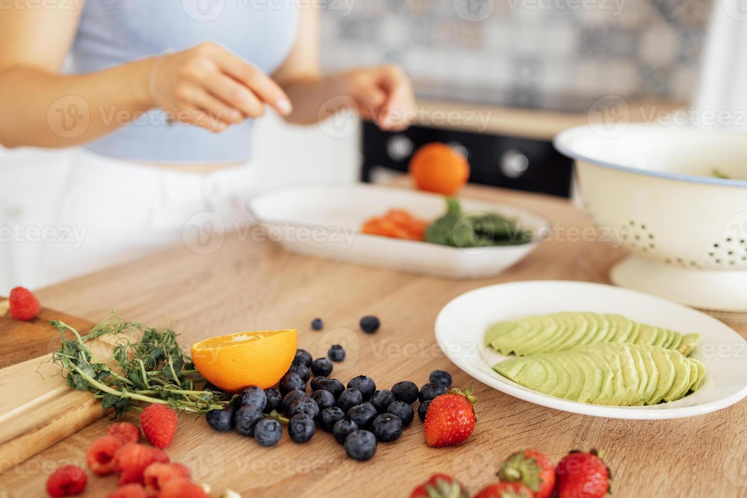 A young girl is preparing a vegan breakfast in the kitchen. Close-up of a plate with avocado, arugula, berries and citrus fruits on a wooden table. photo