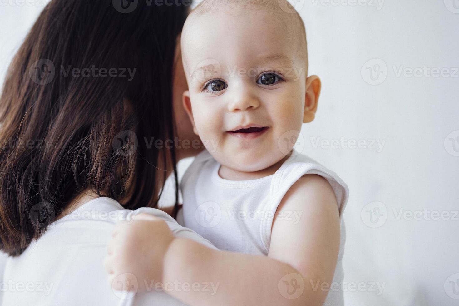 Pretty infant in a white bodysuit with his mom on a light background. Motherhood concept. photo