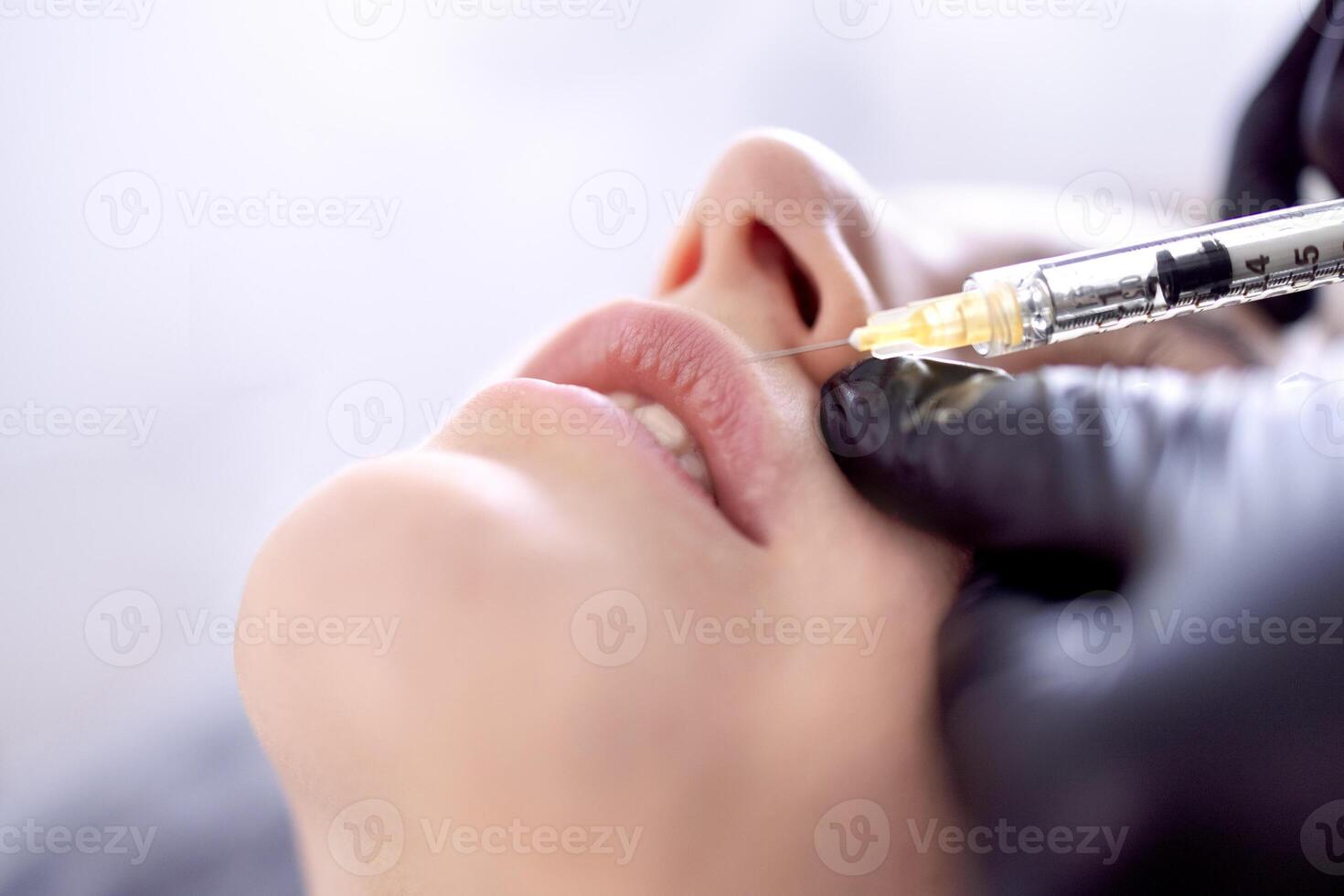Beauty injections. Female cosmetologist in black gloves makes an injection photo
