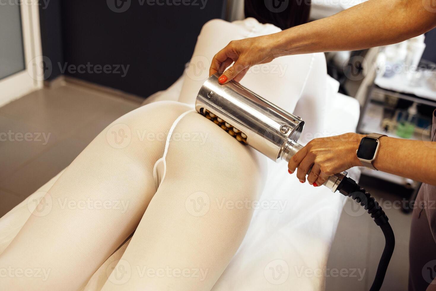 Faceless beautician using massager to remove fat from hips of anonymous customer photo