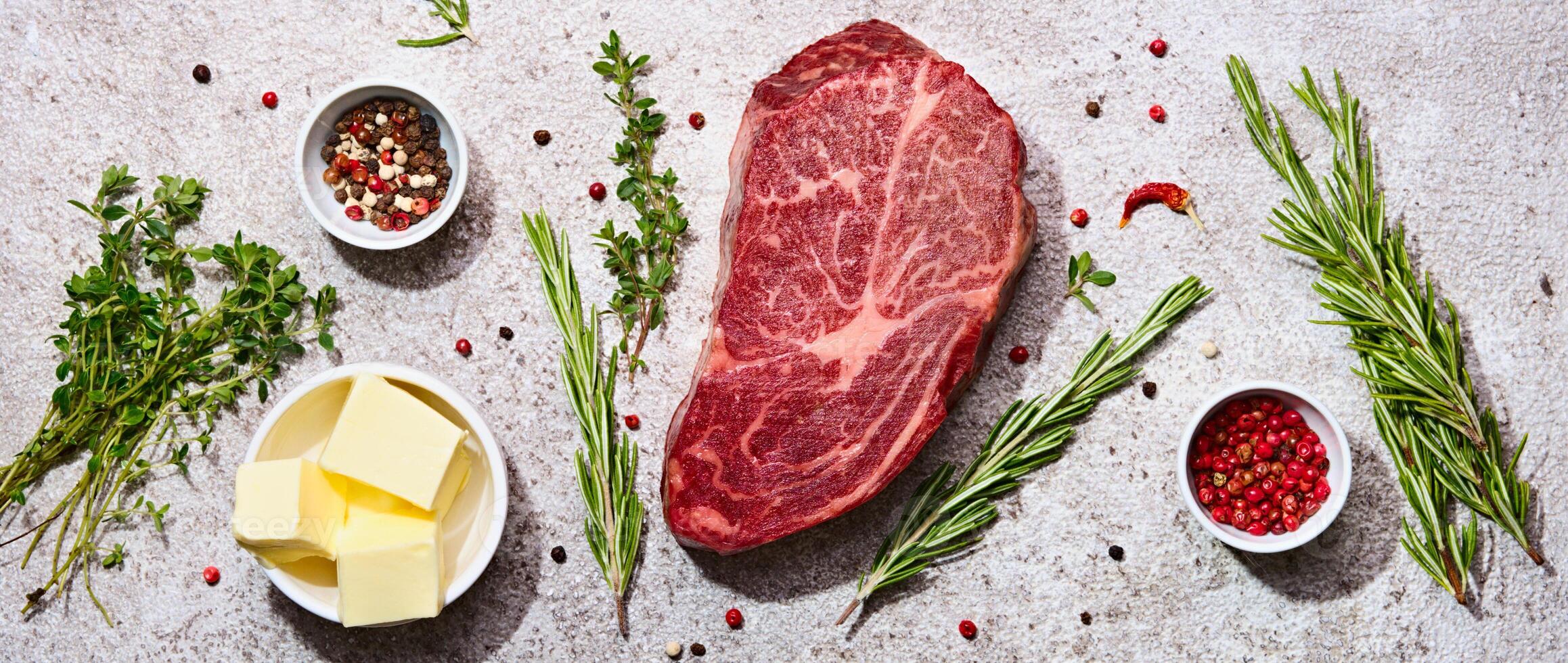 Fresh marbled beef rib eye steak and spices on grey stone background, banner format photo