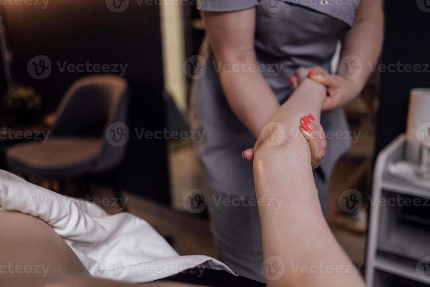Massage therapist with neat manicure and uniform touches woman shoulder and forearm photo