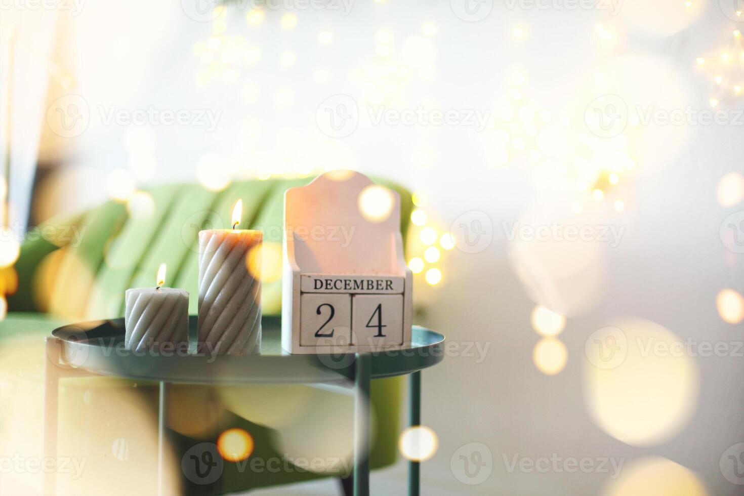 December 24 on wooden calendar standing on small table with burning candles in living room, selective focus. Christmas and New Year concept photo