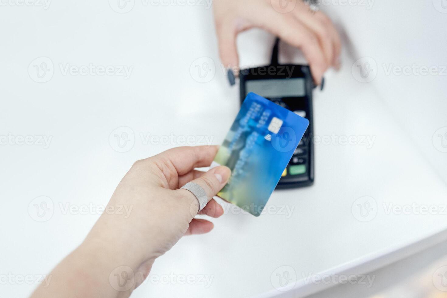Close up of female hand of the client makes contactless payment with bank card. Another womans hand holds payment terminal. photo