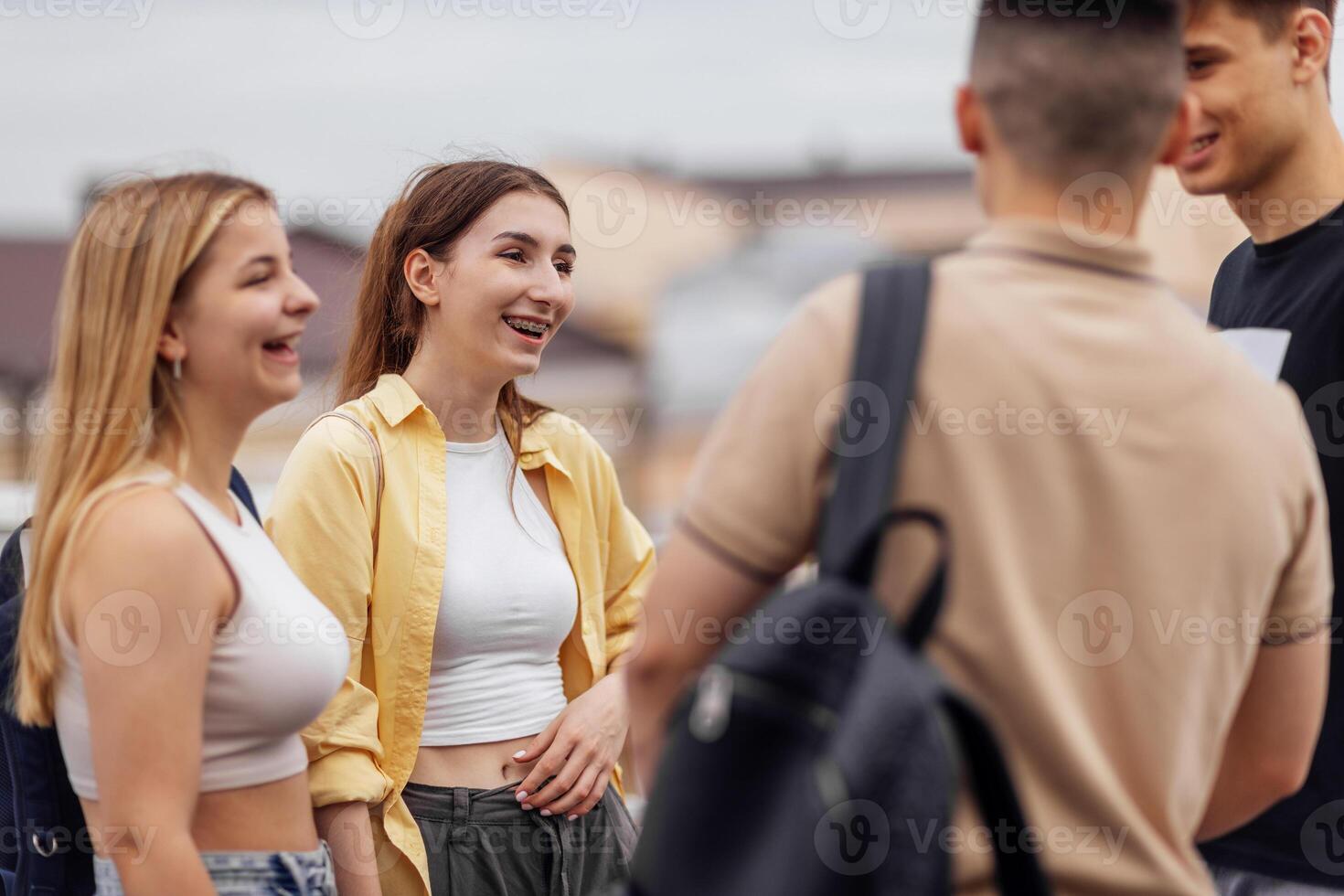 Four teenagers in casual clothes chat and laugh on the roof of the house photo