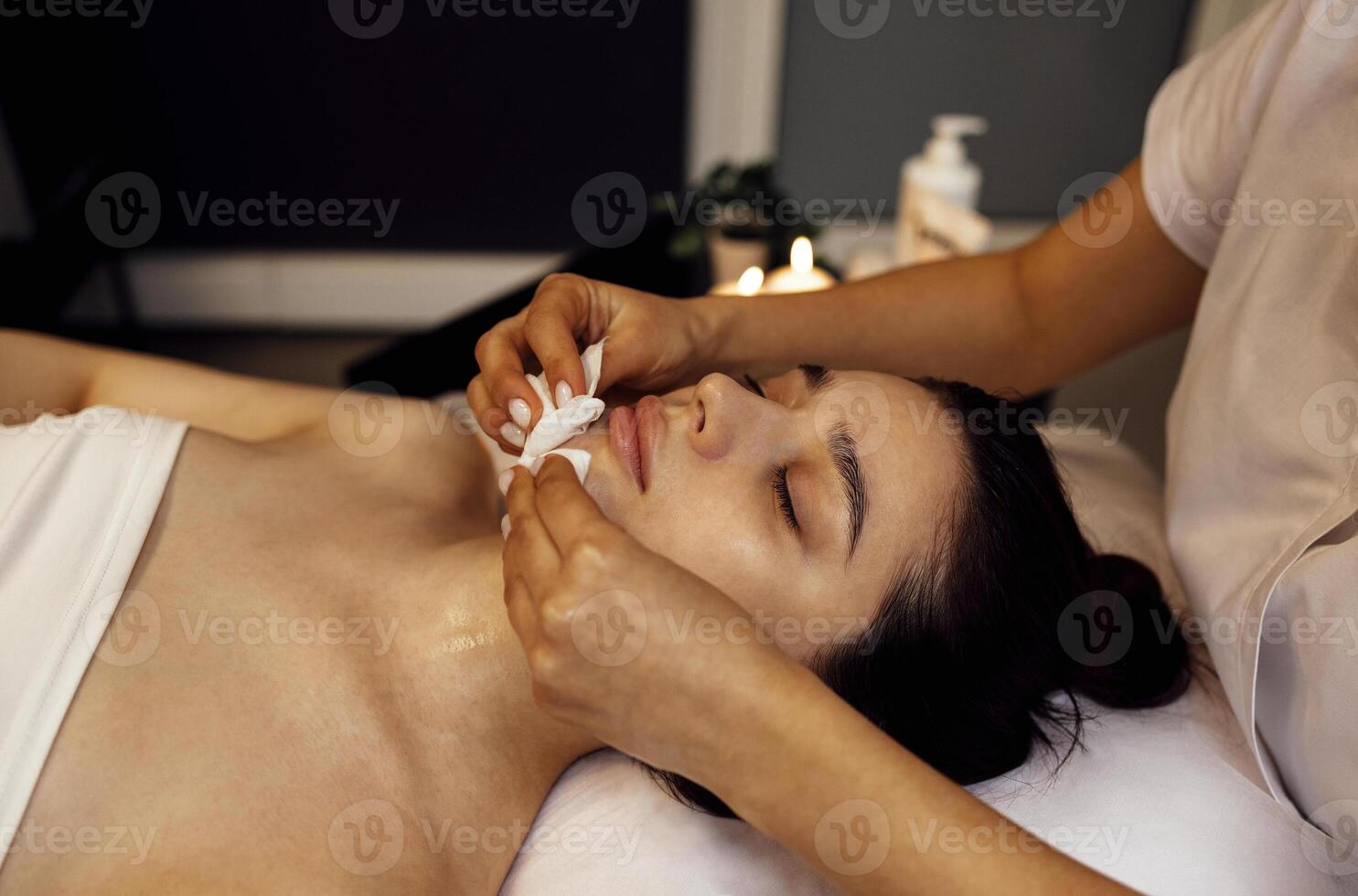 Close up of beautiful young brunette woman during facial cleansing and massage photo