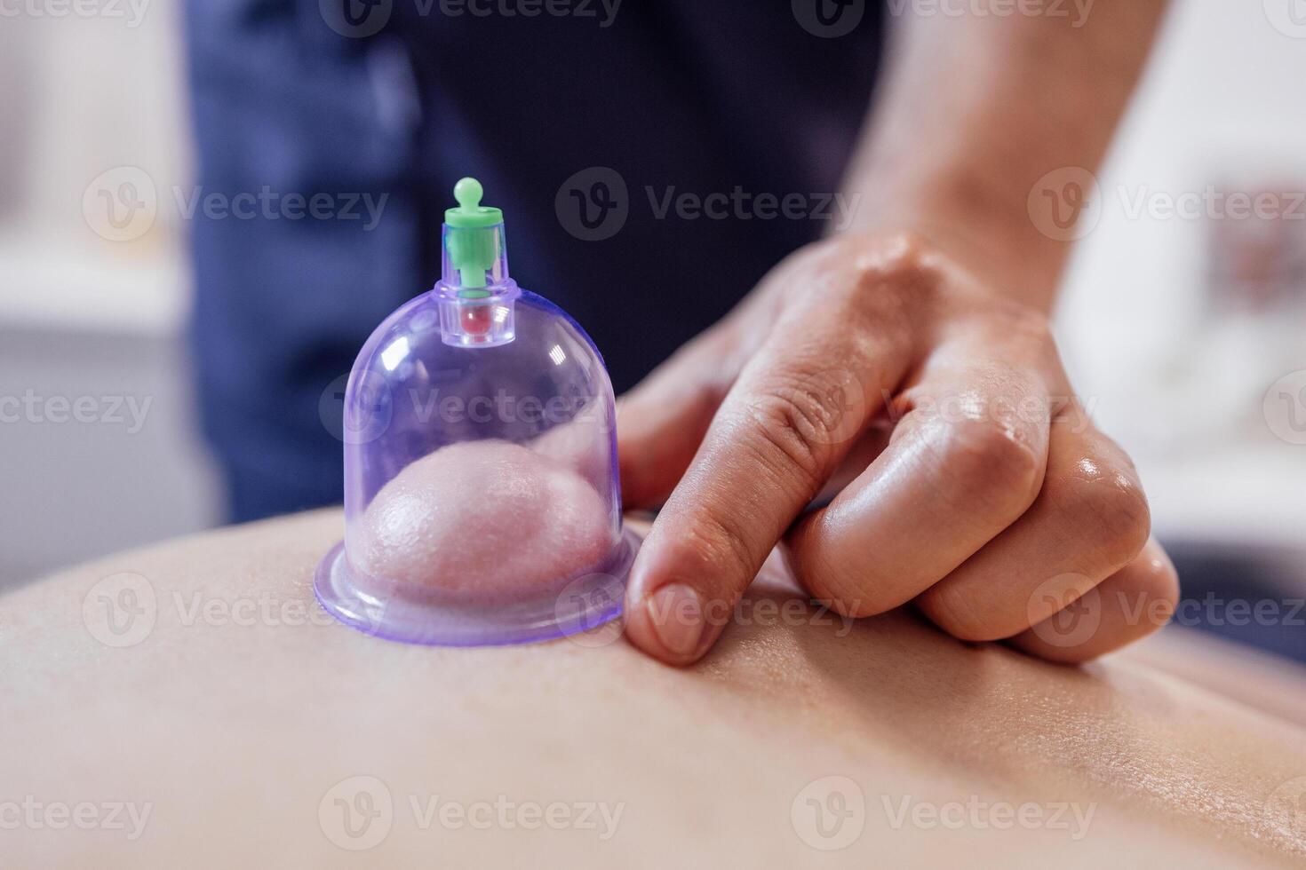 Extrime close up of of the male hand of the masseur putting vacuum healing can on the back of his client. photo
